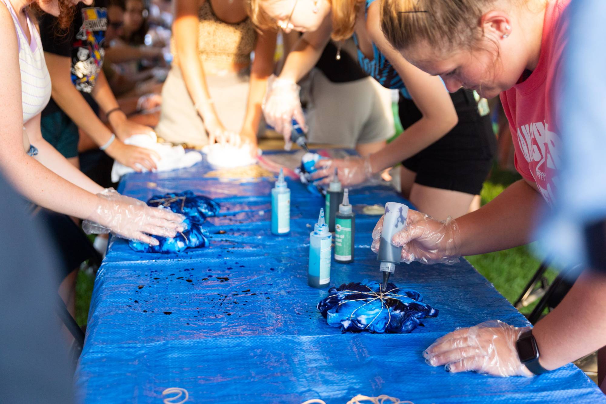 Students gather at a table outside, tie-dying t-shirts